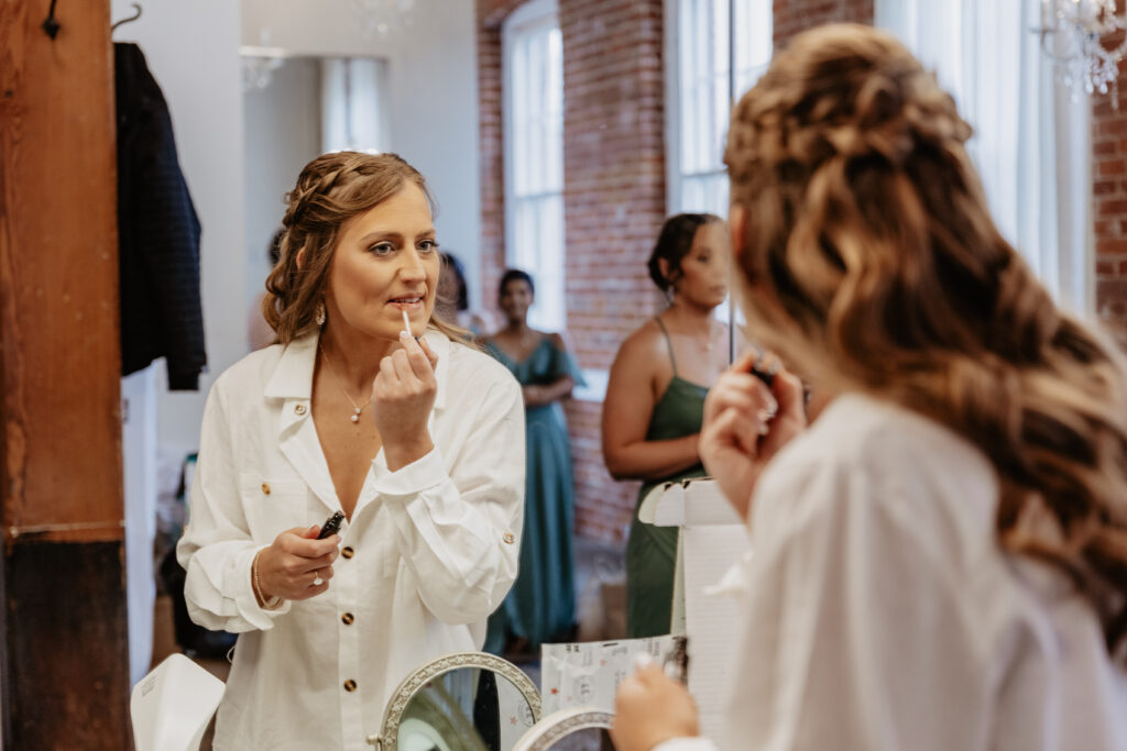 bride getting ready putting on lipgloss in mirror