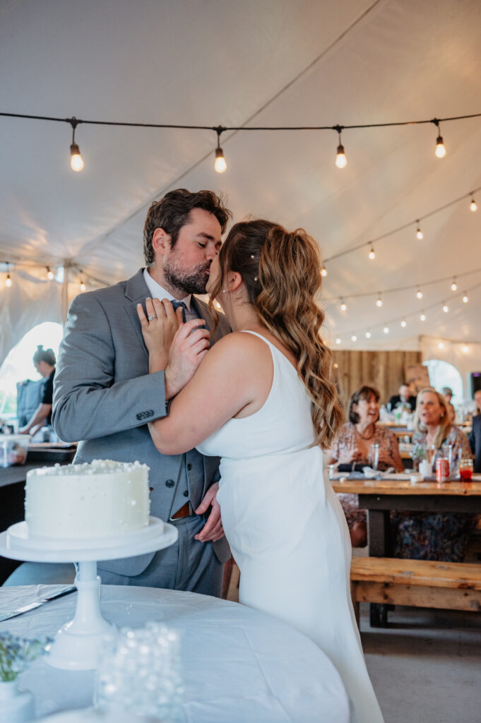 bride and groom kiss during cake cutting at tent wedding