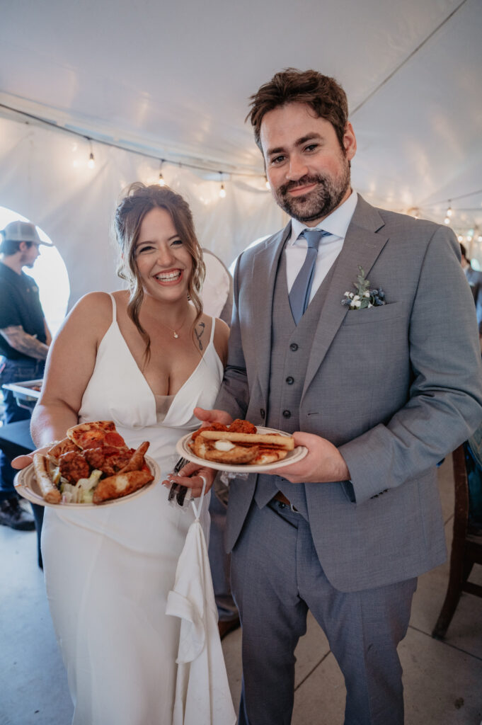 bride and groom smiling holding plates loaded with buffet food