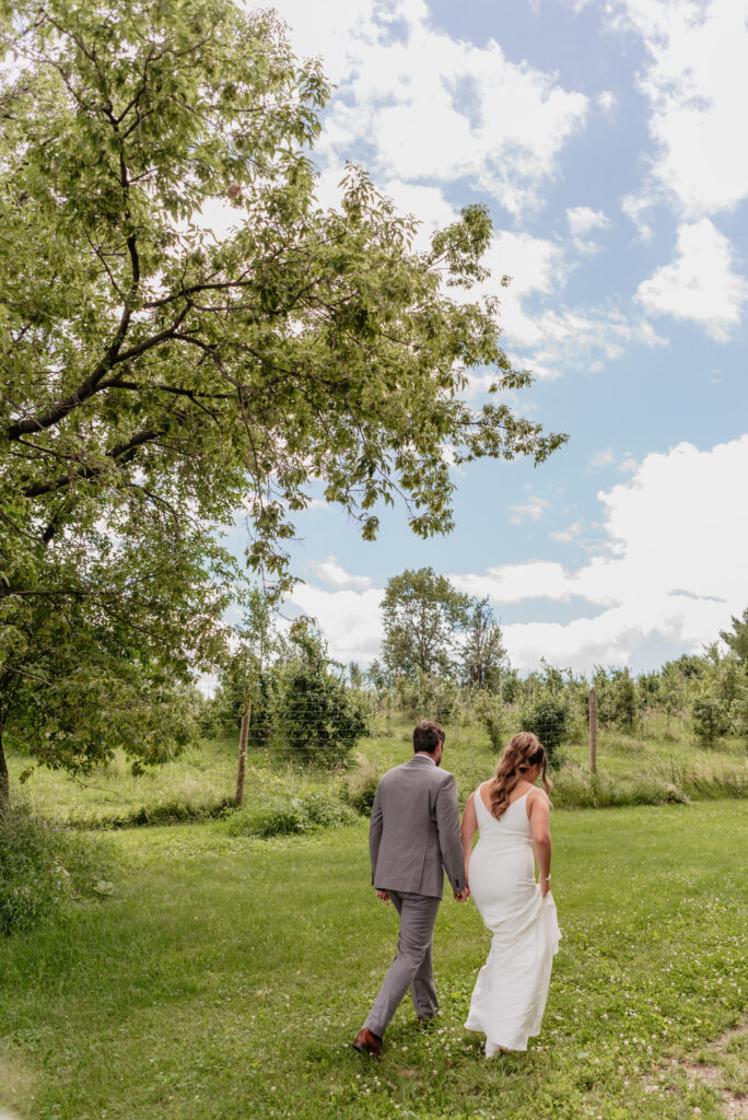 bride and groom walking holding hands through meadow 