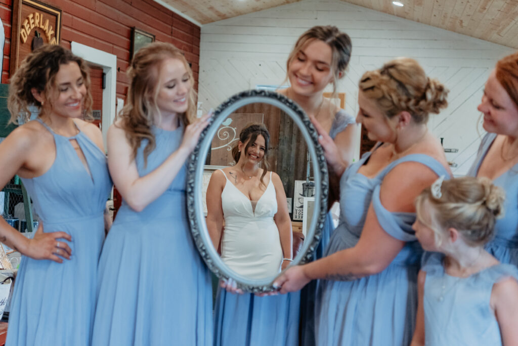 bridesmaids in blue dresses holding mirror to show reflection of bride