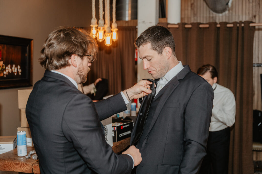 groomsman tying groom's tie getting ready 