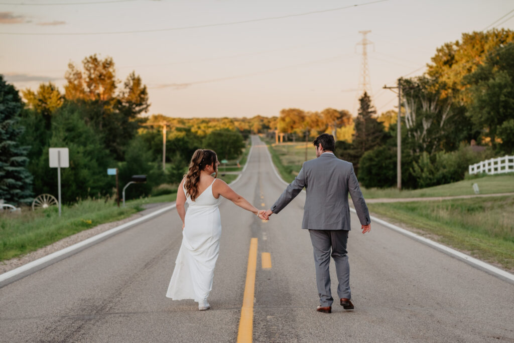 bride and groom holding hands walking down the road for sunset portraits