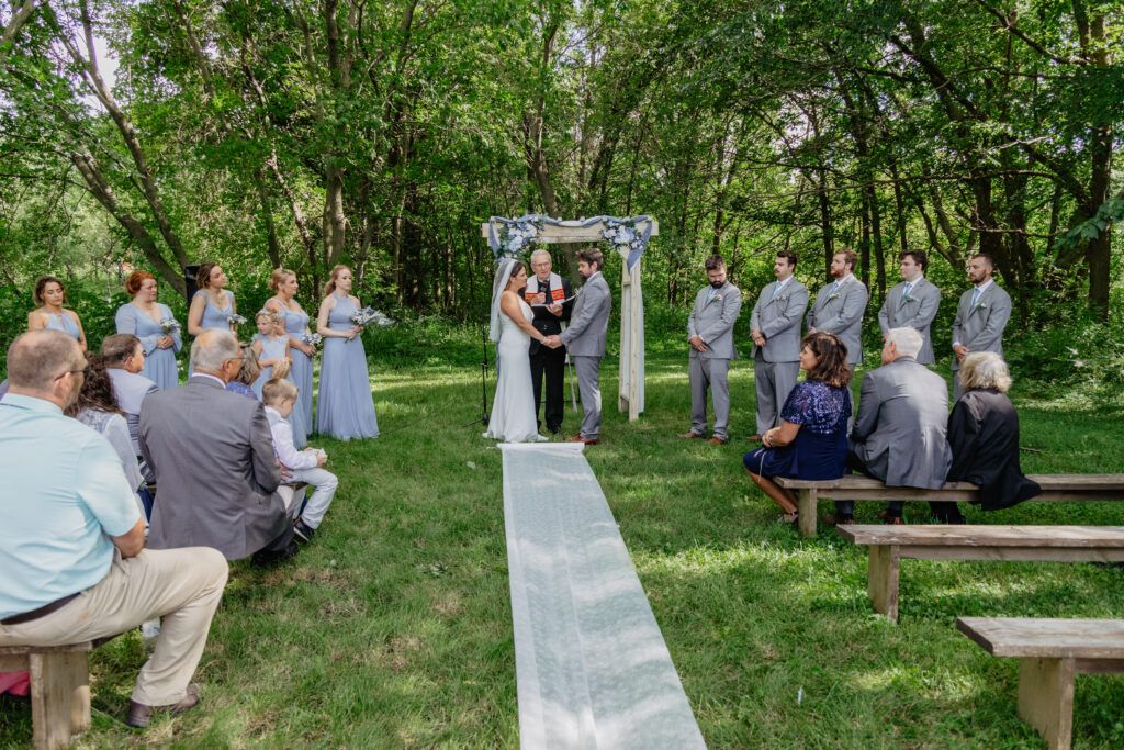 outdoor rustic ceremony site under trees with white aisle runner